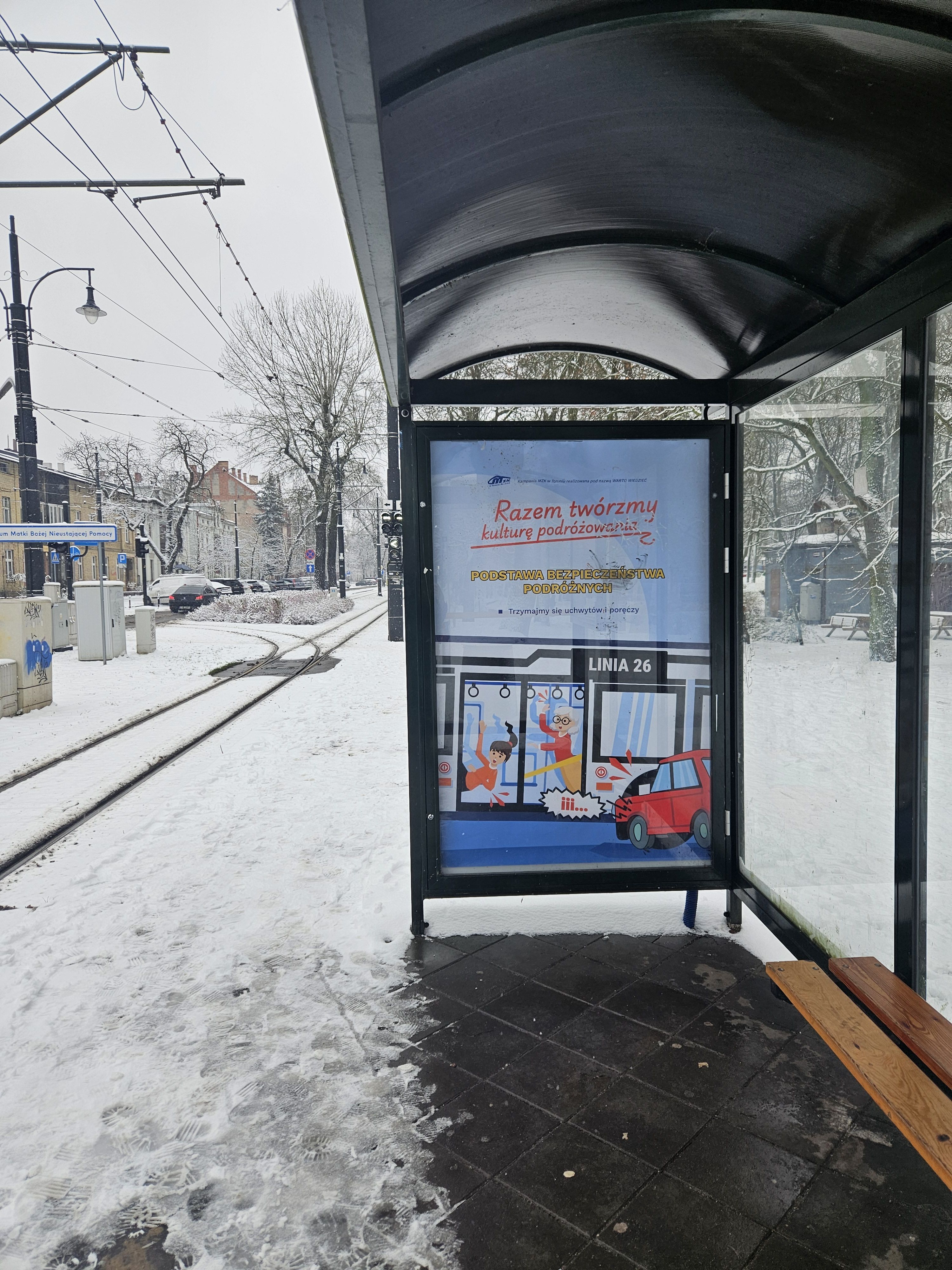Zdjęcie wiaty przystankowej z grafiką nt. trzymania się poręczy w komunikacji miejskiej